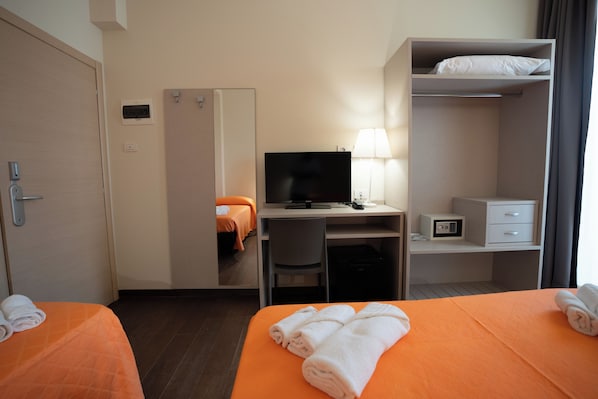A hotel room with two beds, a desk with a computer and lamp, a wardrobe, and a safe.