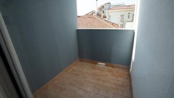 Varanda estreita com piso de azulejos e vista para edifícios vizinhos.