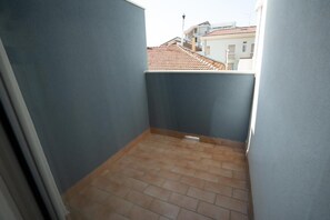 A narrow balcony with tiled flooring and a view of neighboring buildings.
