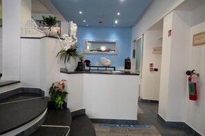 A reception area with a blue accent wall, a reception desk, a mirror, a fire extinguisher, and a staircase. - Hotel Estense (Bellaria-Igea Marina)