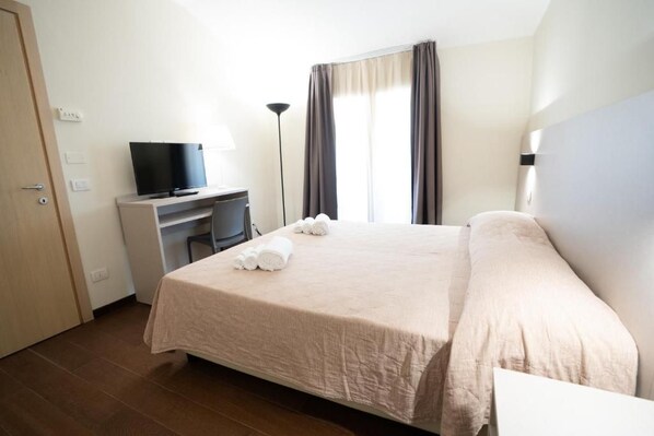 A hotel room with a bed, a desk with a television, and a window with curtains.