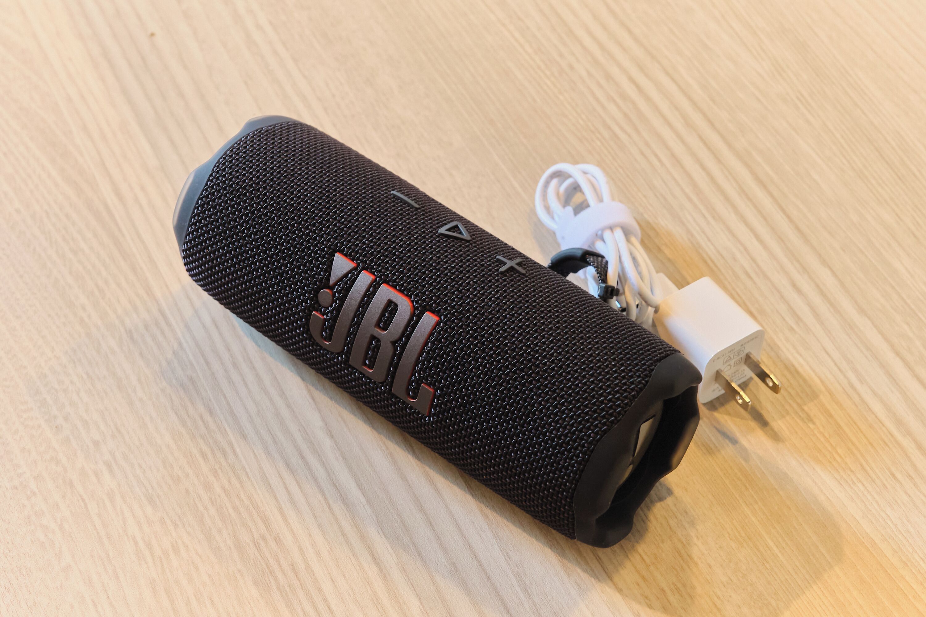A black portable speaker with a visible JBL logo, a power cord, and a white charging adapter.