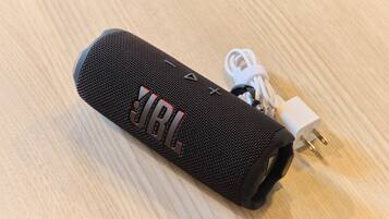 A black portable speaker with a visible JBL logo, a power cord, and a white charging adapter.