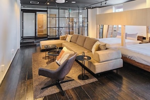 A modern hotel room with a sofa, a chair, a small table, a bed, and a window.