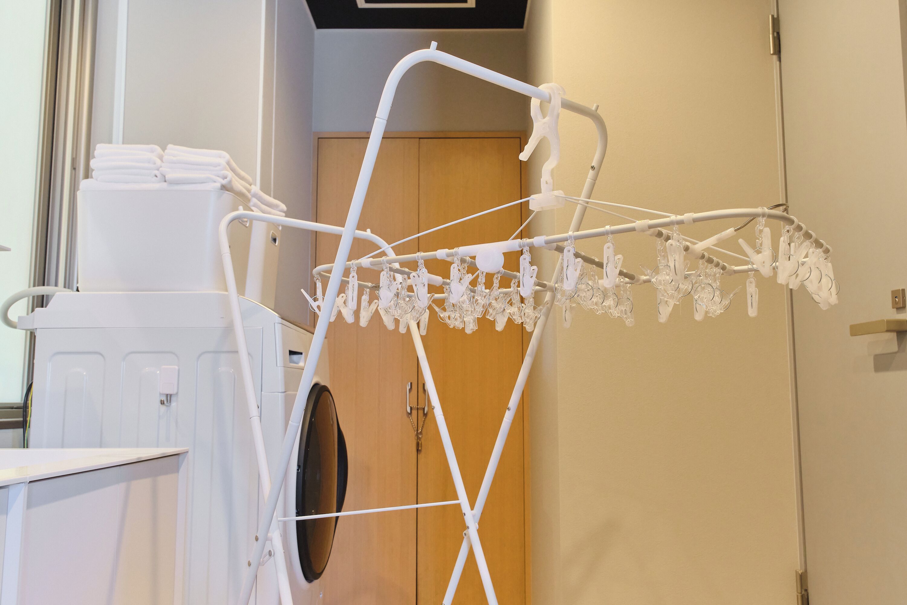 Um varal branco com vários cabides em um quarto com uma porta de madeira e um eletrodoméstico branco.