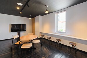 A conference room with a round table, six chairs, a flat-screen TV, and a large window.