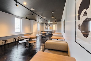 A modern interior with multiple seating areas, including tables and booths, and a large window providing natural light.