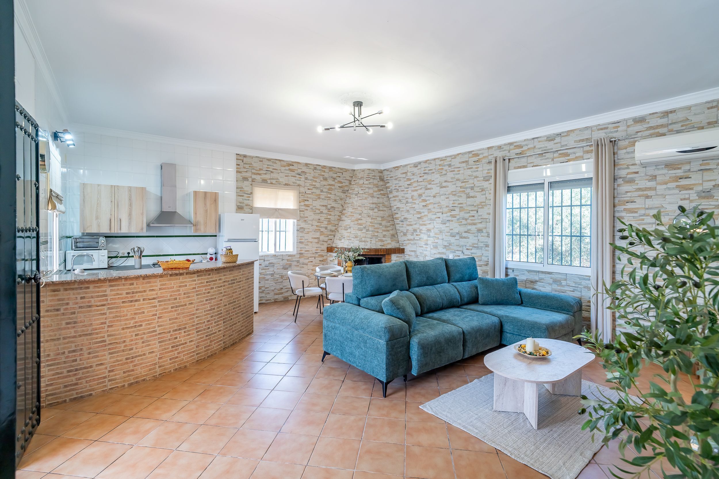 Una cocina moderna con una isla central, un comedor con mesa y sillas, un sofá azul y una pequeña mesa blanca.