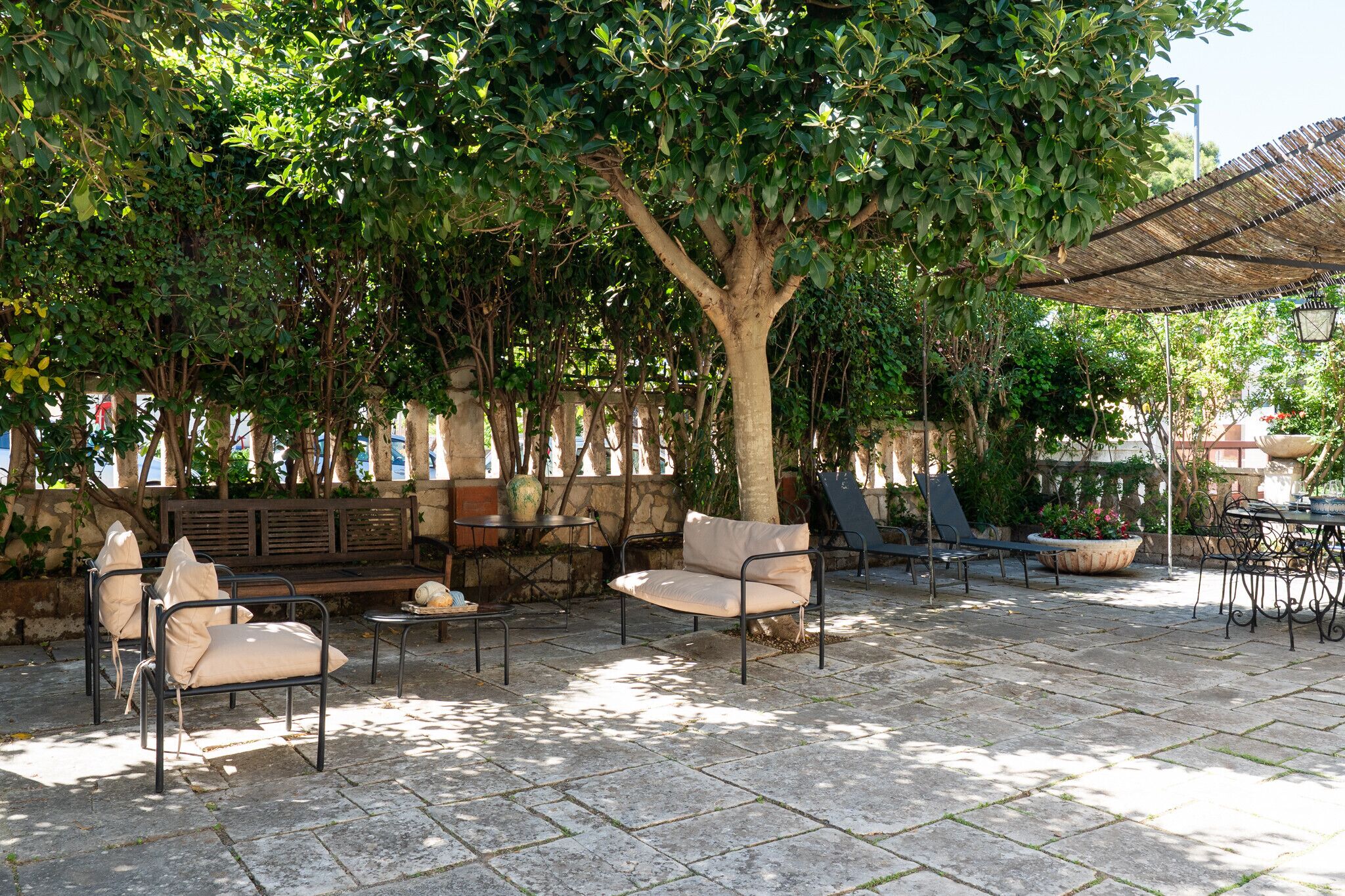 An outdoor patio with seating, a table, and a large tree providing shade.