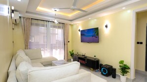 A modern living room with a sofa set, a flat-screen TV, ceiling fan, and a small plant. - Radium Residences View Palace Apartment (Mombasa)