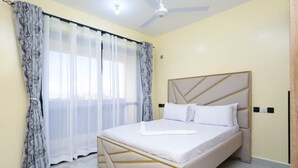 A bedroom with a bed, curtains, a ceiling fan, and a light fixture. - Radium Residences View Palace Apartment (Mombasa)