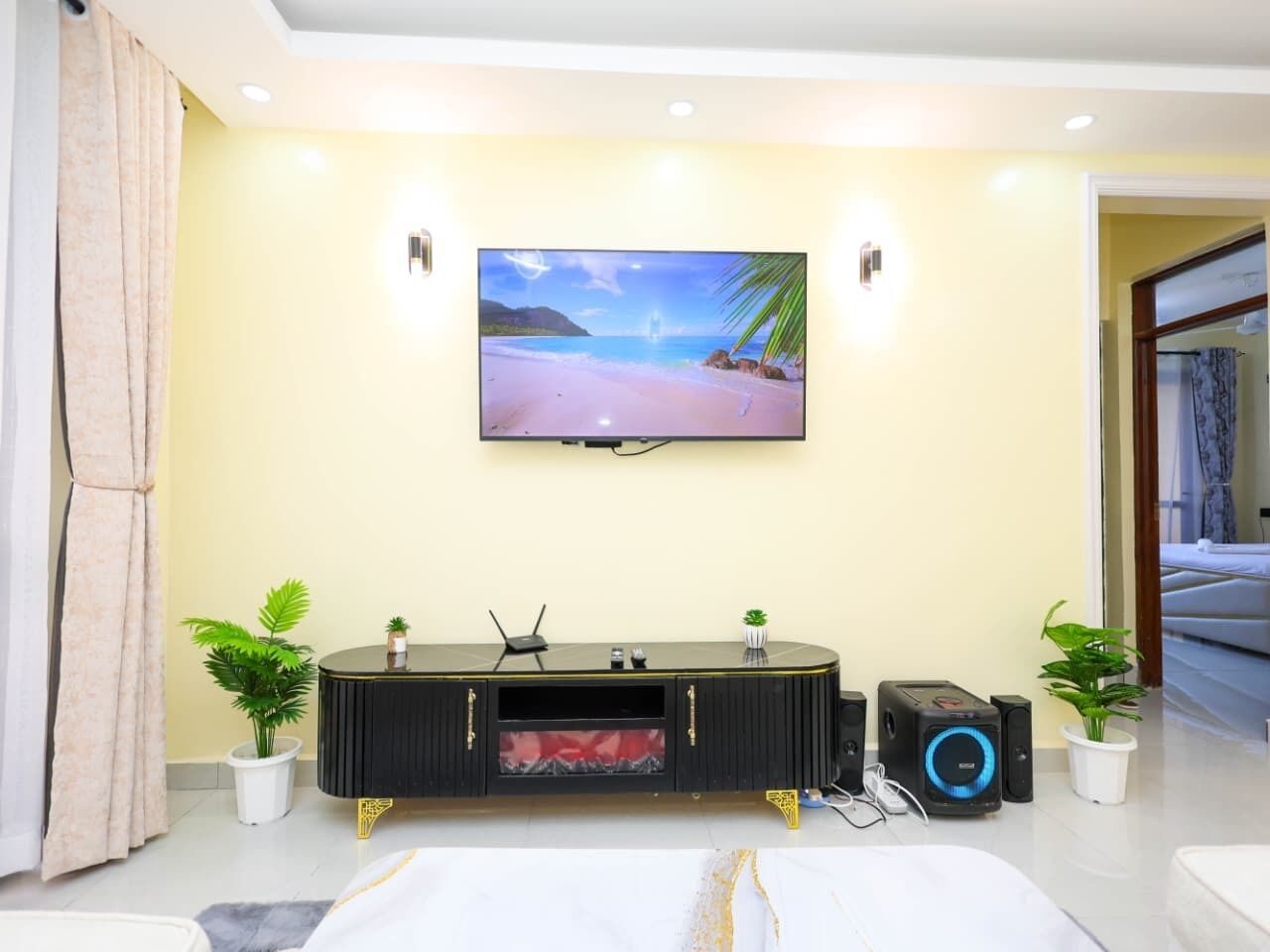 Una sala de estar moderna con un televisor de pantalla plana, un mueble de entretenimiento negro, dos plantas en macetas y una cama.