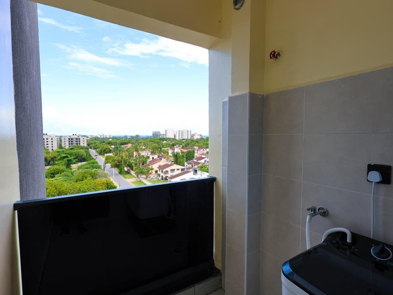 A bathroom with a toilet, a sink, and a shower. There is a window with a view of a residential area.