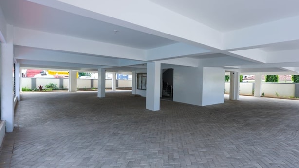 An indoor space with a brick floor and white walls, featuring a central open area with pillars and a visible exit. - Radium Residences View Palace Apartment (Mombasa)