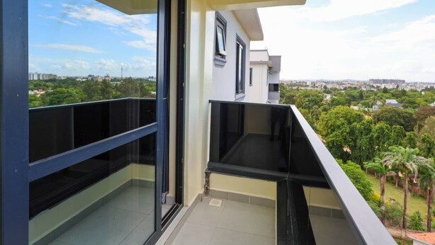 A balcony with a glass door, a black railing, and a view of a cityscape and greenery. - Radium Residences View Palace Apartment (Mombasa)