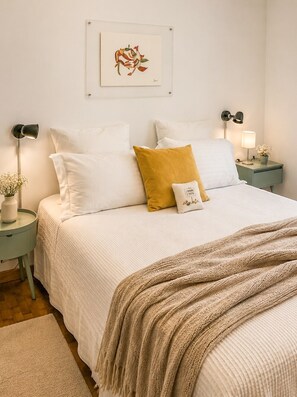 Ein ordentlich eingerichtetes Schlafzimmer mit einem Bett, Kissen, einem Nachttisch mit Lampe, einem Wandbild und einer Stehlampe.