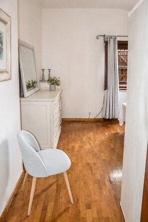 Ein Zimmer mit Holzboden, einem weißen Kommoden, einem Stuhl, einem Spiegel und einem Fenster mit Vorhängen.