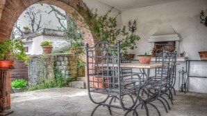 En udendørs terrasse med et jernbord og stole, plantekasser og en murstensvæg.