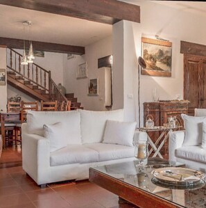 Ein geräumiges Wohnzimmer mit einem weißen Sofa, einem Glastisch und einer Holztreppe.