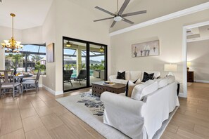 A spacious living room with a white sofa, a coffee table, and a chandelier. - Waterfront Home + Heated Pool + Spa + Dock | Minutes to Beach | Neptune's Realm (Marco Island)