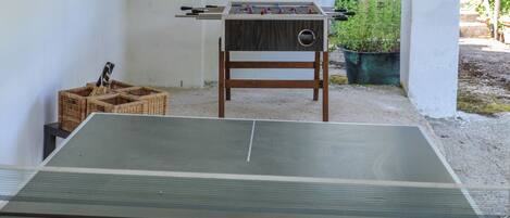 A ping pong table with a dartboard and foosball table in a room with white walls and a brick archway.