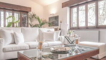 A modern living room with a white sofa, a glass coffee table, and large windows.