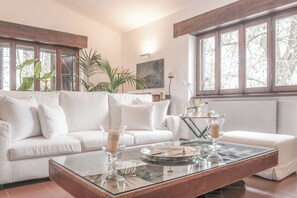 Ein modernes Wohnzimmer mit einem weißen Sofa, einem Glastisch und großen Fenstern.