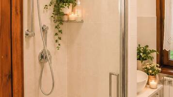 A shower with a glass door, a potted plant, and a shelf with candles.