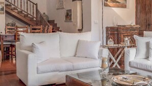 A spacious living room with a white sofa, a glass coffee table, a wooden staircase, and a painting on the wall. - Il Casale dei Castagni (Caprarola)