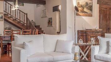 A spacious living room with a white sofa, a glass coffee table, a wooden staircase, and a painting on the wall.