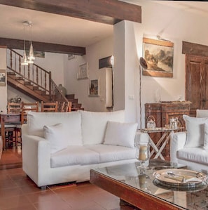 Ein geräumiges Wohnzimmer mit einem weißen Sofa, einem Glastisch, einer Holztreppe und einem Bild an der Wand.