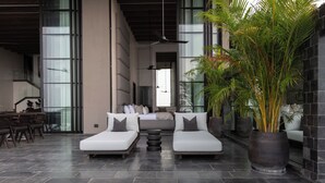 Un área de estar moderna con dos sofás blancos, una planta grande en maceta y un comedor con sillas y mesas.