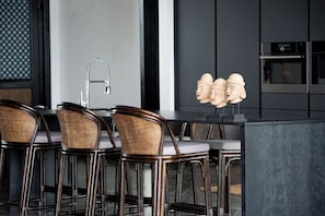 Una cocina moderna con un salpicadero oscuro, electrodomésticos de acero inoxidable y una zona de bar con sillas de mimbre.