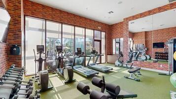 Un gimnasio con equipo de ejercicios, ventanas amplias y una pared de ladrillo.