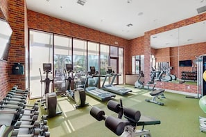 A gym with exercise equipment, large windows, and a brick wall. - Luxury Kissimmee Resort Escape ~ Disney ~ Pool! (Kissimmee)