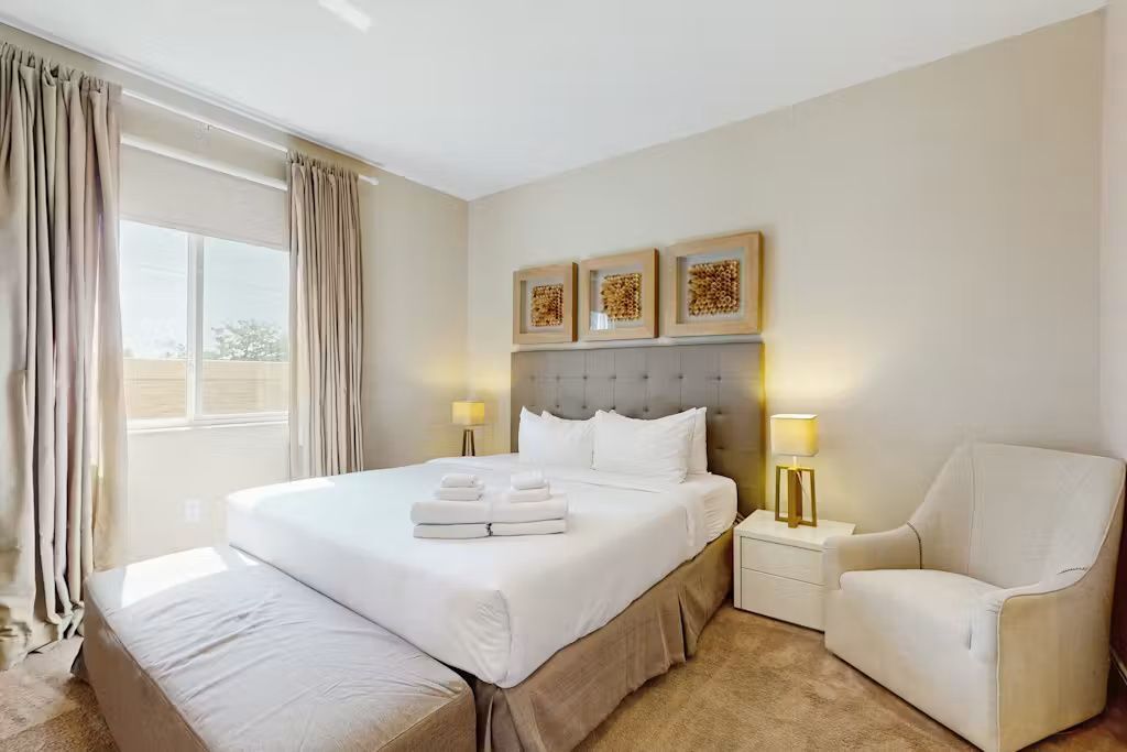 Una habitación de hotel con una cama grande, mesitas de noche, una silla y una obra de arte en la pared.