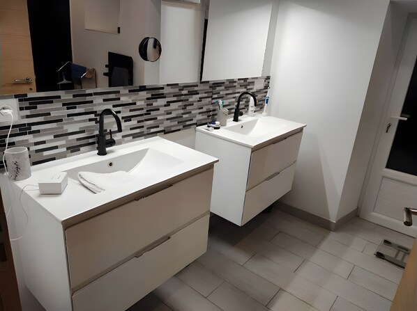 A modern bathroom with two sinks, a mirror, and a tiled backsplash.