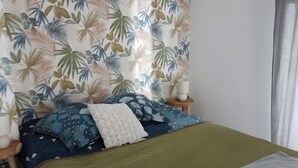 A bedroom with a bed, pillows, a green blanket, a headboard with a leaf pattern, and a white lamp on the nightstand.