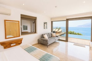 A modern living room with a sofa, a wooden cabinet, a large window, and a view of the sea. - Villa Ayışığı (Kaş)