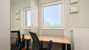 Ein Zimmer mit einem Holztisch, zwei schwarzen Bürostühlen, einem Fenster mit Jalousien und einem weißen Heizkörper.