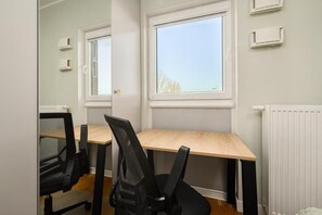A room with a wooden table, two black office chairs, a window with blinds, and a white radiator. - ShortStayPoland Szwedzka B109 (Warszawa)