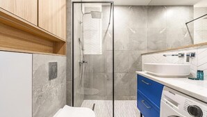 Ein modernes Badezimmer mit einer gläsernen Duschkabine, einer weißen Toilette, einer Waschmaschine und einem Waschbecken mit Spiegel darüber.