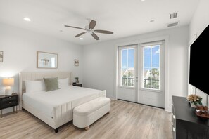 A bedroom with a bed, nightstand, bench, ceiling fan, and a view through the door. - Sleeps 26 • 2 Coastal Homes • 1 Block To Beach + Pool + Hot Tub | Twin Tides (Panama City Beach)