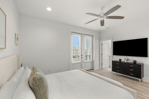 Ein Schlafzimmer mit Bett, Deckenventilator, Fernseher und einer Tür, die auf einen Balkon führt.