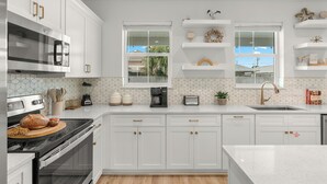 A modern kitchen with white cabinetry, a built-in oven, a microwave, and a coffee maker. - Sleeps 26 • 2 Coastal Homes • 1 Block To Beach + Pool + Hot Tub | Twin Tides (Panama City Beach)