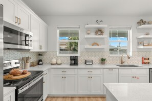 A modern kitchen with white cabinetry, a built-in oven, a microwave, and a coffee maker. - Sleeps 26 • 2 Coastal Homes • 1 Block To Beach + Pool + Hot Tub | Twin Tides (Panama City Beach)