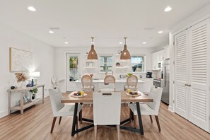 A modern kitchen with white cabinetry, a dining table with chairs, pendant lights, and a view into the adjacent dining area. - Sleeps 26 • 2 Coastal Homes • 1 Block To Beach + Pool + Hot Tub | Twin Tides (Panama City Beach)
