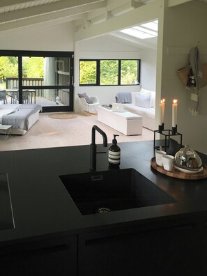A modern kitchen with a black countertop, a sink, and a dining area with a table and chairs. - Architect-designed 80s house by Hornbæk (Hornbæk)