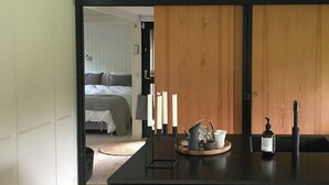 A modern kitchen with a central island, wooden panel walls, and a visible bedroom in the background. - Architect-designed 80s house by Hornbæk (Hornbæk)