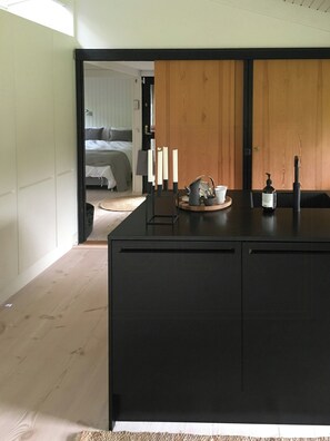 A modern kitchen with a central island, wooden panel walls, and a visible bedroom in the background. - Architect-designed 80s house by Hornbæk (Hornbæk)
